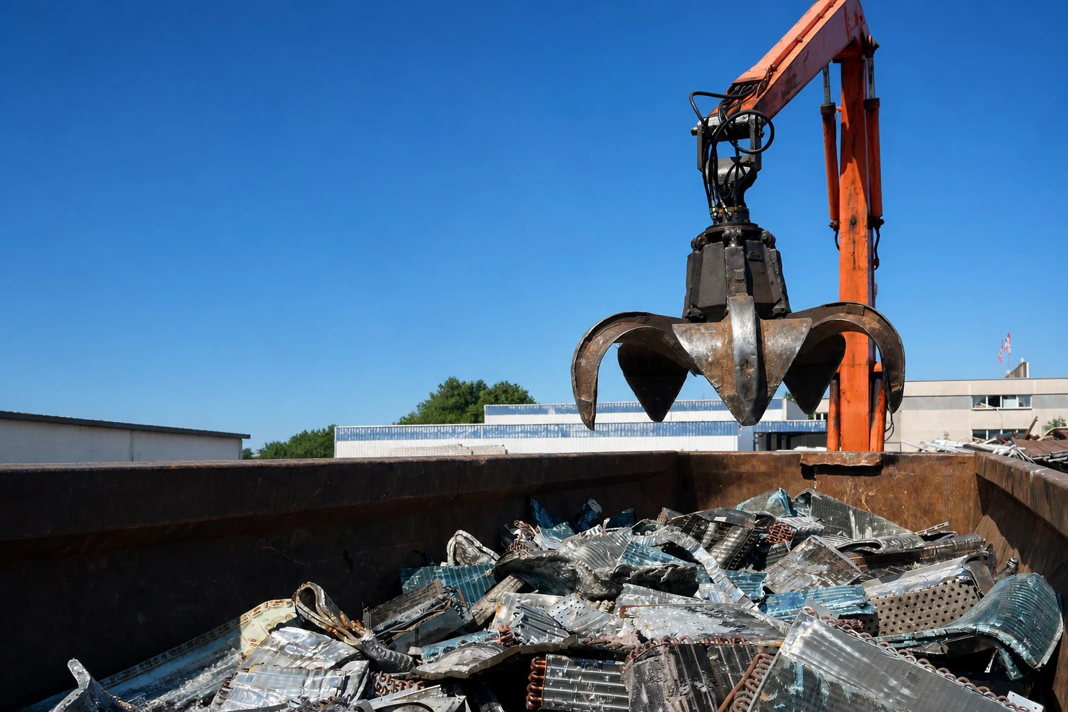 Bagger mit Metallgreifer über einem mit Metallschrott gefüllten Container